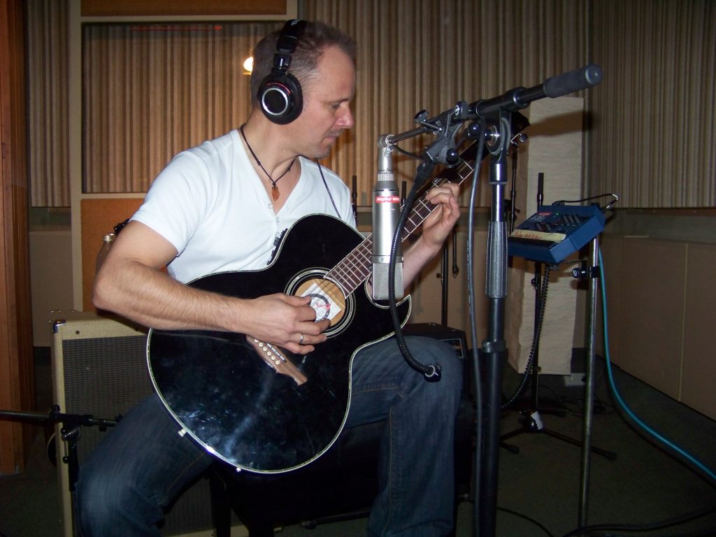 Joey Krüger mit schwarzer Akustikgitarre und Kopfhörern im Studio, mikrofoniert für eine Aufnahme